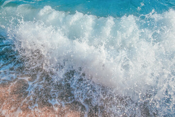 Fototapeta premium Ocean wave crashing onto sandy beach, creating foam and splashes, with clear blue water and sunlight reflecting on the surface in a tropical setting