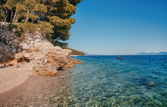 Scenic coastal view featuring clear turquoise water, rocky shoreline, and lush green trees under a bright blue sky in a serene natural environment