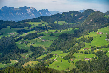 Obraz premium Panoramic view of the Tyrolean Alps in Austria, with rolling green hills, forests, mountain farms and dramatic peaks in the distance.
