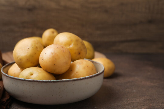 Ripe raw young potatoes in bowl on brown table, closeup. Space for text