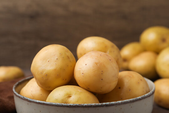 Ripe raw young potatoes in bowl on brown table, closeup. Space for text