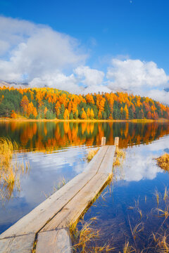 Vertical photo. Lake and a small pier. Autumn landscape. Clouds and fall forest. Incredible view of the mountain valley with lake. Background, wallpaper, postcards