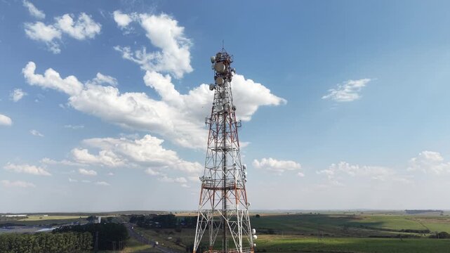Aerial view of a tall telecommunications tower with antennas against a blue sky with clouds