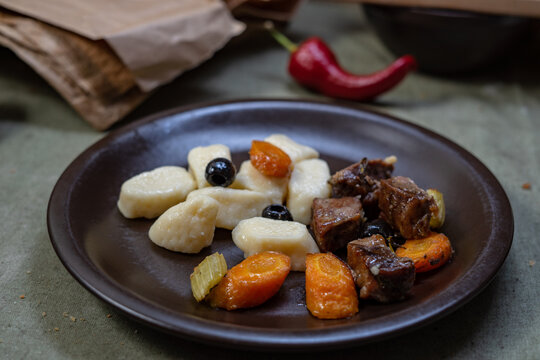 Traditional potato gnocchi served with slow cooked meat stew and vegetables on dark plate