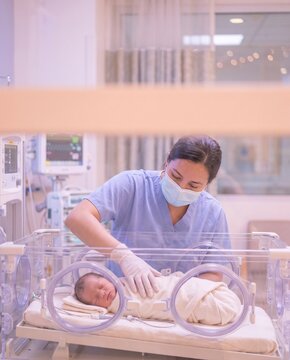 Compassionate pediatric nurse resting hand beside premature baby in modern incubator for maternity care guide