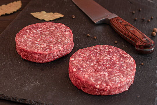 Raw minced meat patties for burgers prepared for cooking on dark board