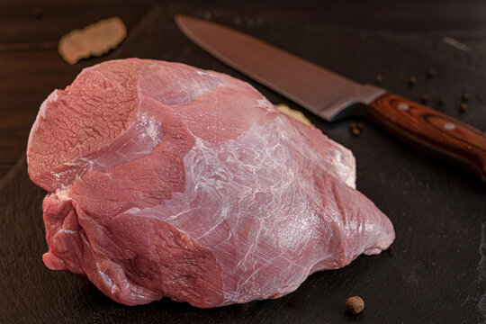 Fresh raw pork meat cuts with bay leaves and peppercorns on dark wooden board