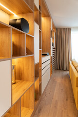 A modern living room interior with warm wooden shelving and integrated lighting, minimalist storage cabinets and a yellow sofa, creating a cozy, organized and stylish home atmosphere.  © Manual Mood