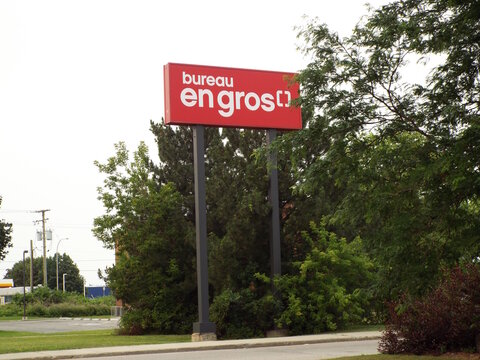 Gatineau, Quebec, Canada &ndash; July 07, 2026: An outdoor view showing a red "Bureau en Gros" store sign standing on tall poles amidst trees and greenery on Mnt Paiement.