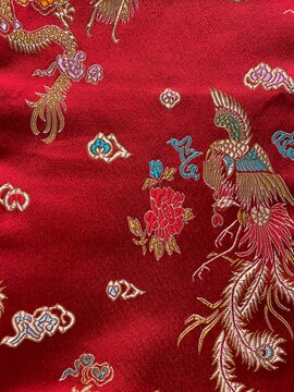 Close-up of authentic Chinese red silk fabric with intricate traditional embroidery of phoenix, dragon motifs, peony flowers and cloud patterns in gold, blue and purple threads 