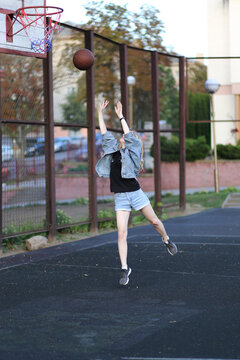 Blonde woman in jeans and denim shorts shooting a basketball on an outdoor court