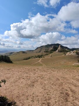 Dirt Track Through Rolling Grassland and Rocky Hills Beneath White Clouds