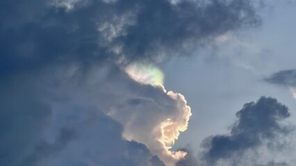Obraz premium Iridescent cloud formation displaying soft rainbow colors against a backdrop of deep dark stormy skies