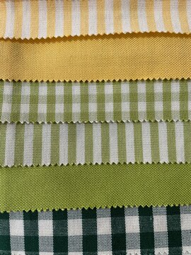 Assortment of fabric swatches featuring yellow and green striped, gingham, and solid patterns stacked in rows 