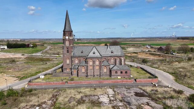brick steeple towers over manheim alt hamlet ruins scattered houses grass reclaims empty foundations kerpen germany open pit lignite mine wind turbines line distant horizon aerial orbit drone footage