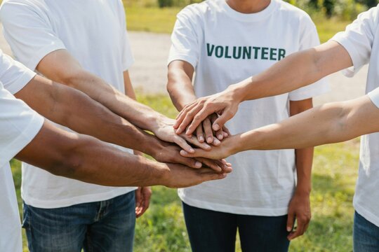 Diverse volunteers stacking their hands together in unity outdoors. Community service concept for teamwork presentations.