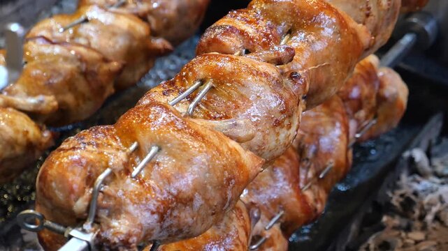 Rows of whole rotisserie chickens rotating on spits over glowing coals close up