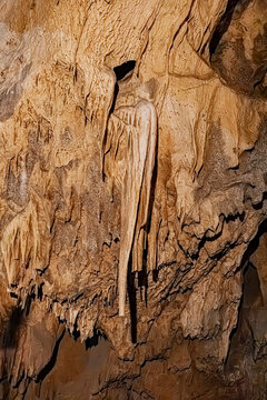 Flowstone formation and wall-hugging stalactite along an ochre-colored cave wall, Pyrenees, France