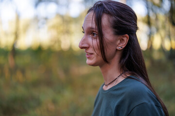 A close-up profile portrait of a brunette woman smiling outdoors in a autumn park with soft blurred background lighting © WoodHunt