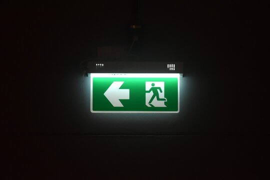 close up of green electric light box sign fire exit door on wall in black background