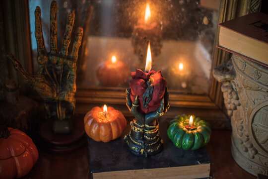 Cozy Halloween home decor with burning pumpkin candles, handmade heart candle, vintage books and mystical props on table