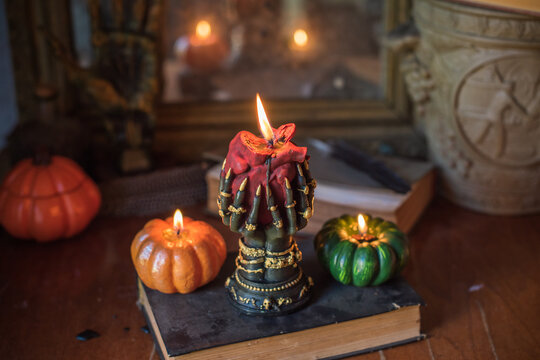 Cozy Halloween home decor with burning pumpkin candles, handmade heart candle, vintage books and mystical props on table