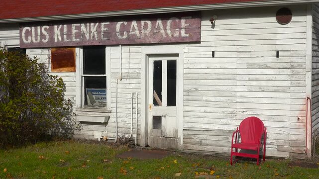 Rustic vintage garage building with faded signage and lonely red outdoor chair in quiet countryside setting.