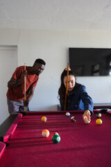 Fototapeta premium Couple playing pool on burgundy felt table at home, lining shot near billiard balls and cues
