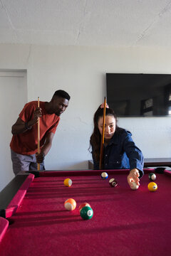 Couple playing pool on burgundy felt table at home, lining shot near billiard balls and cues