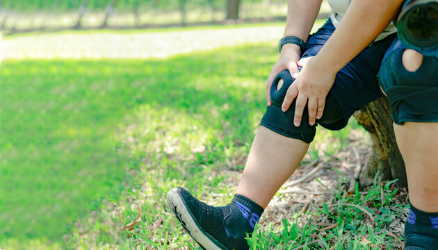 Overweight man wearing knee brace was experiencing worrisome pain in his right knee joint sore and swollen could barely walk sat and rested under tree gently massag.