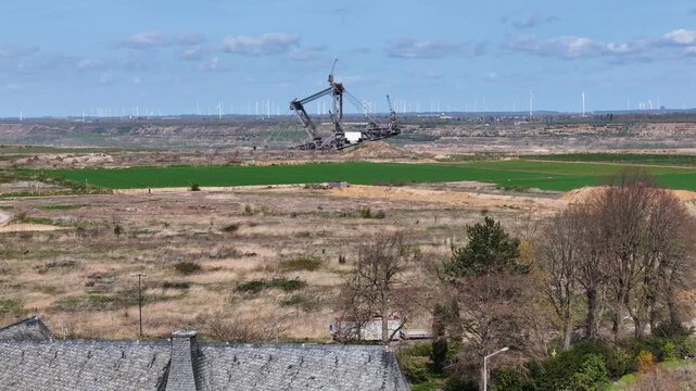bucket wheel excavator dominates hambach lignite mine cleared farmland kerpen germany church rooftop foreground wind turbines line distant horizon open pit mining site aerial telephoto drone shot