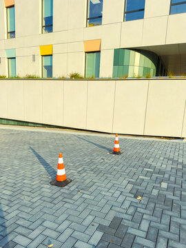 Traffic cones mark a section of paving near a building with colorful windows in a clear outdoor setting during daylight hours