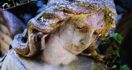 Naklejka premium Close-up of a weathered mourning angel statue covered with moss and traces of decay, symbolic image of grief, mortality, remembrance and the passage of time.
