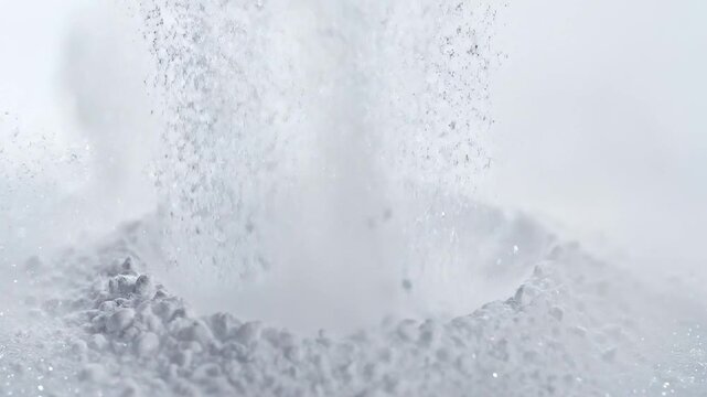 A makeup brush dips into loose powder creating a small cloud of powder. This happens indoors in a well-lit place. The brush has soft bristles and moves gently