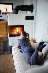 Obraz premium Woman relaxing indoors on sofa, watching fire and holding wine, warm home environment and peaceful evening lifestyle moment