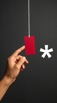 Hand holding a red tag against a dark backdrop, with a white asterisk symbol nearby, suggesting a sale or emphasis, ideal for promotions.