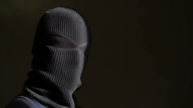 Masked person wearing knitted balaclava in a dark room with concealed identity