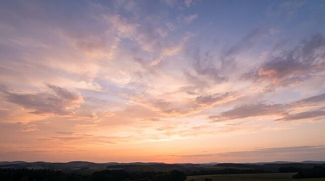 Beautiful sunset sky with soft pink and orange clouds over a dark landscape horizon at dusk