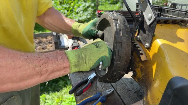 Gardener mounting new wheel onto lawn mower chassis in backyard.