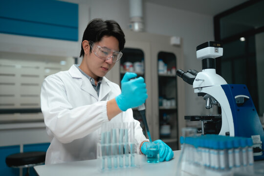 Young Asian scientist using pipette to fill test tubes with blue liquid in laboratory
