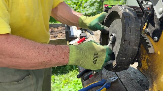 Man inspecting and adjusting wheel mechanism on yellow petrol lawn mower.