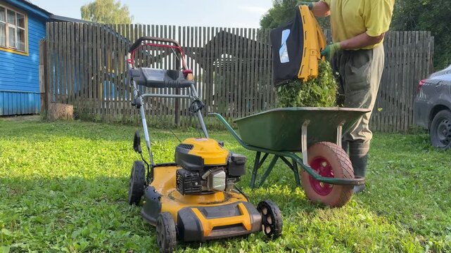Man emptying grass catcher bag from lawn mower into garden wheelbarrow.