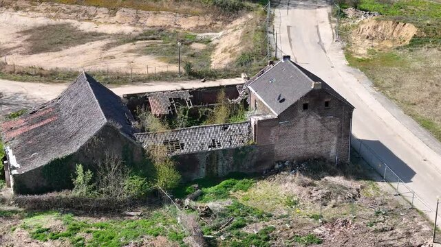 second derelict farmhouse sits beside first ivy climbs cracked brick walls sagging roof partially caved scattered debris fills overgrown yard chain link fence lines roadside drone footage orbit