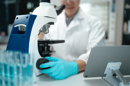 Scientist adjusting microscope focus with gloved hand in modern laboratory setting during research
