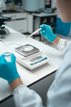 Scientist wearing blue gloves weighing white powder sample on precision scale in laboratory