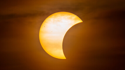 Partial solar eclipse on September 12, 2026, with the Moon visibly covering a significant portion of the Sun. The Sun appears as a bright orange crescent against a dark sky.  © coffeinlix 