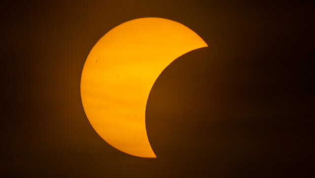Partial solar eclipse on September 12, 2026, with the Moon visibly covering a significant portion of the Sun. The Sun appears as a bright orange crescent against a dark sky. 