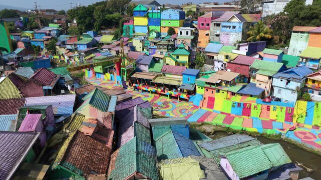 Aerial drone view of colorful Jodipan Village in Malang, Indonesia, showing brightly painted houses along the river. Vibrant urban neighborhood and popular tourist attraction.