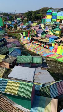 Aerial drone view of colorful Jodipan Village in Malang, Indonesia, showing brightly painted houses along the river. Vibrant urban neighborhood and popular tourist attraction.