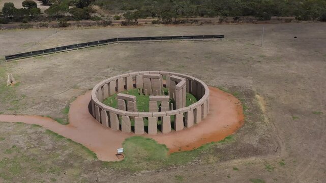Aerial view of a replica of stonehenge in a rural Australian field showing circular stone monument under blue sky.